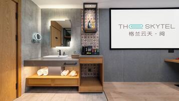 A modern bathroom with a large mirror, a sink, and a shower area. There is a wooden cabinet with towels and toiletries.