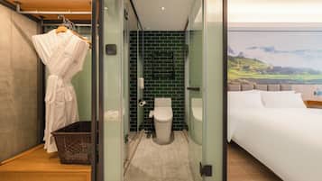 A modern hotel room with a glass shower enclosure, a white bed, and a view of a mountainous landscape.