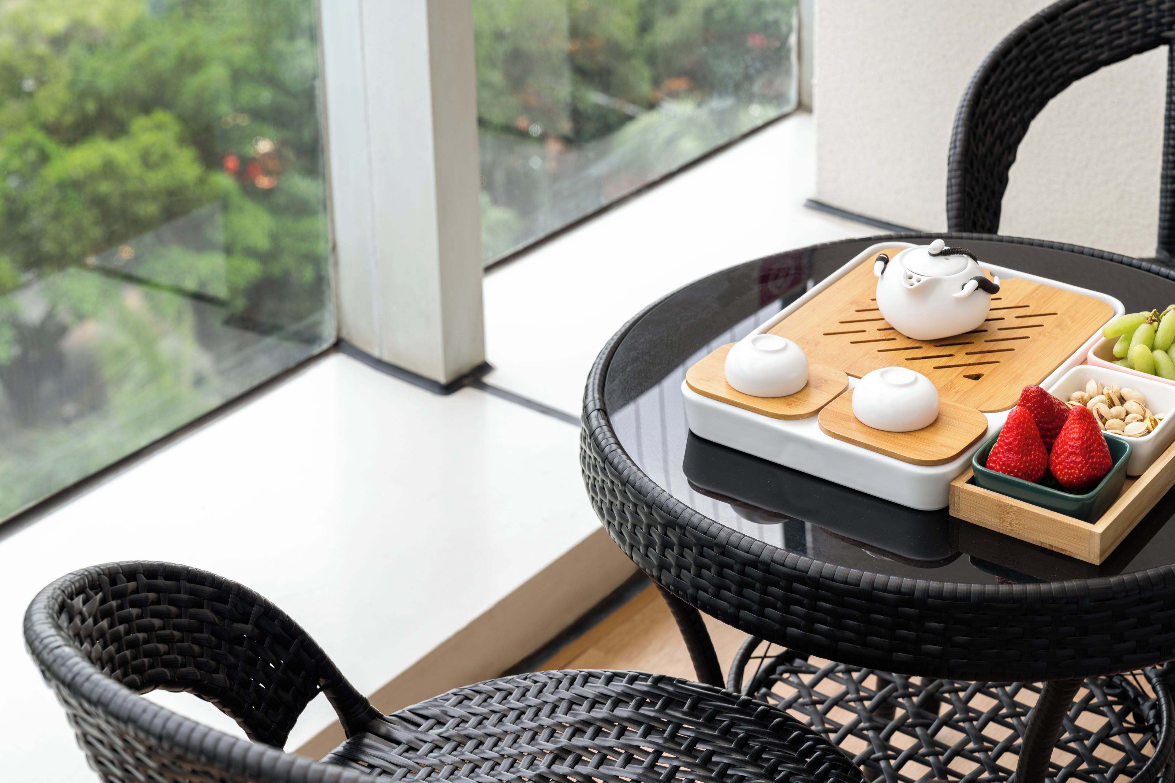 A round table with a teapot, two cups, a tray with grapes and nuts, and a wicker chair.