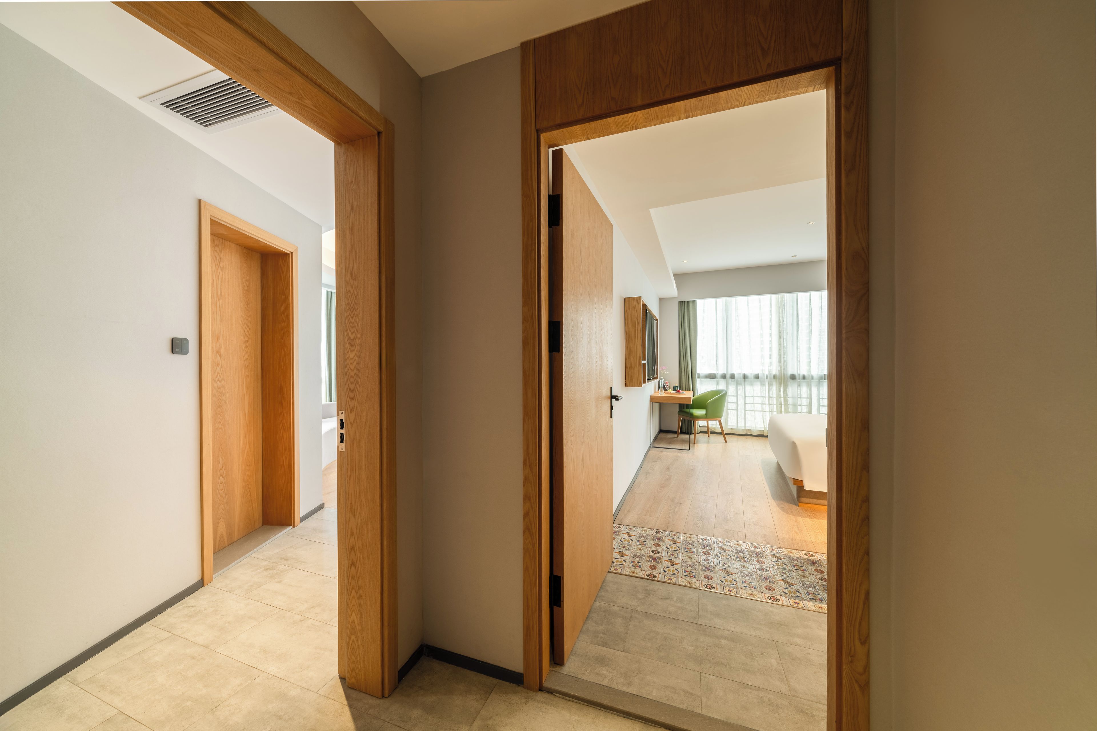 A hallway with a wooden door leading to a room with a bed and a desk.
