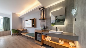 Et moderne hotelværelse med seng, skrivebord, lille køleskab, sminkebord med spejl og et vindue med gardiner.