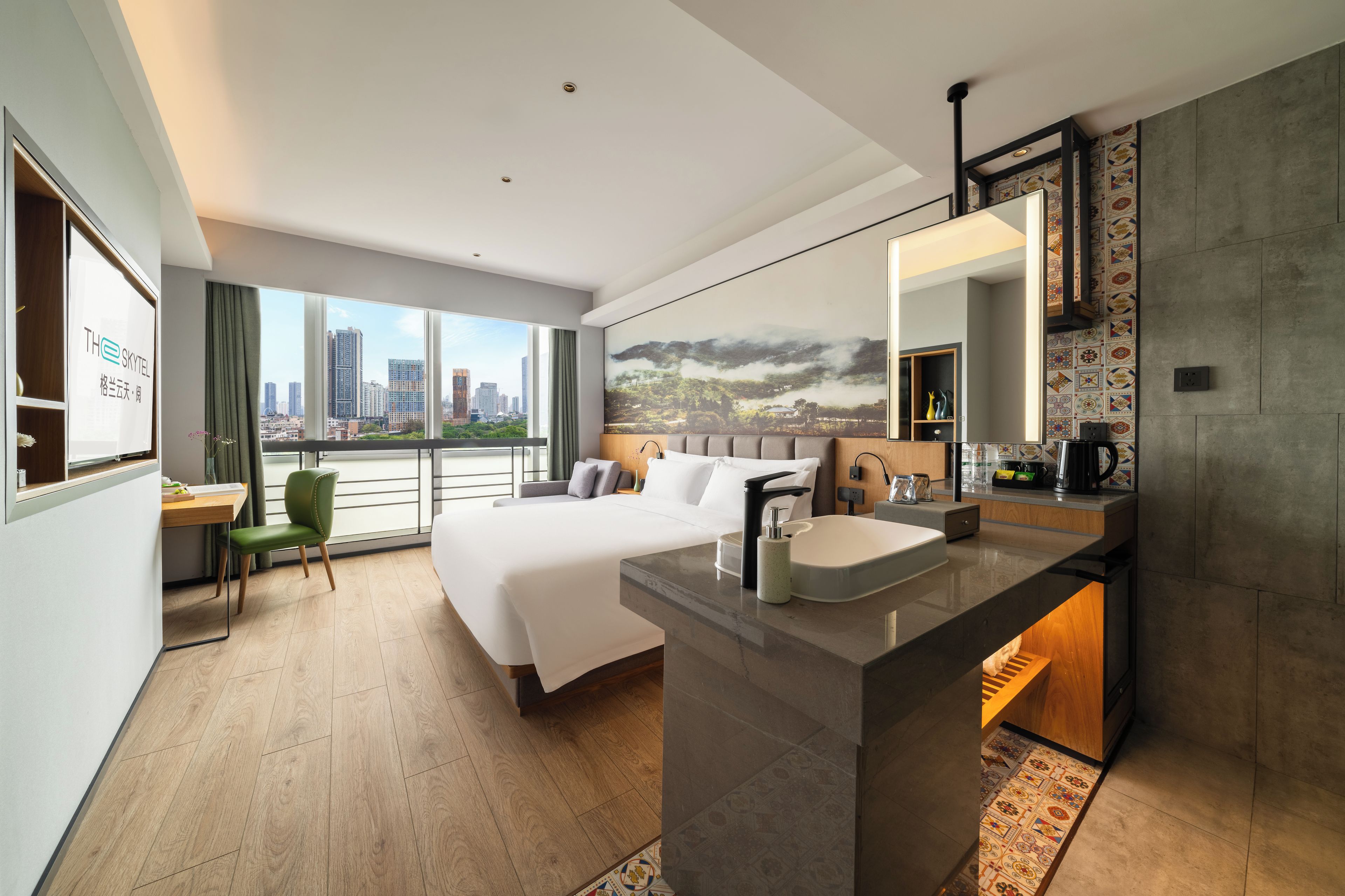 A modern hotel room with a large bed, a desk, a chair, a bathroom with a sink and mirror, and a city view through the window.