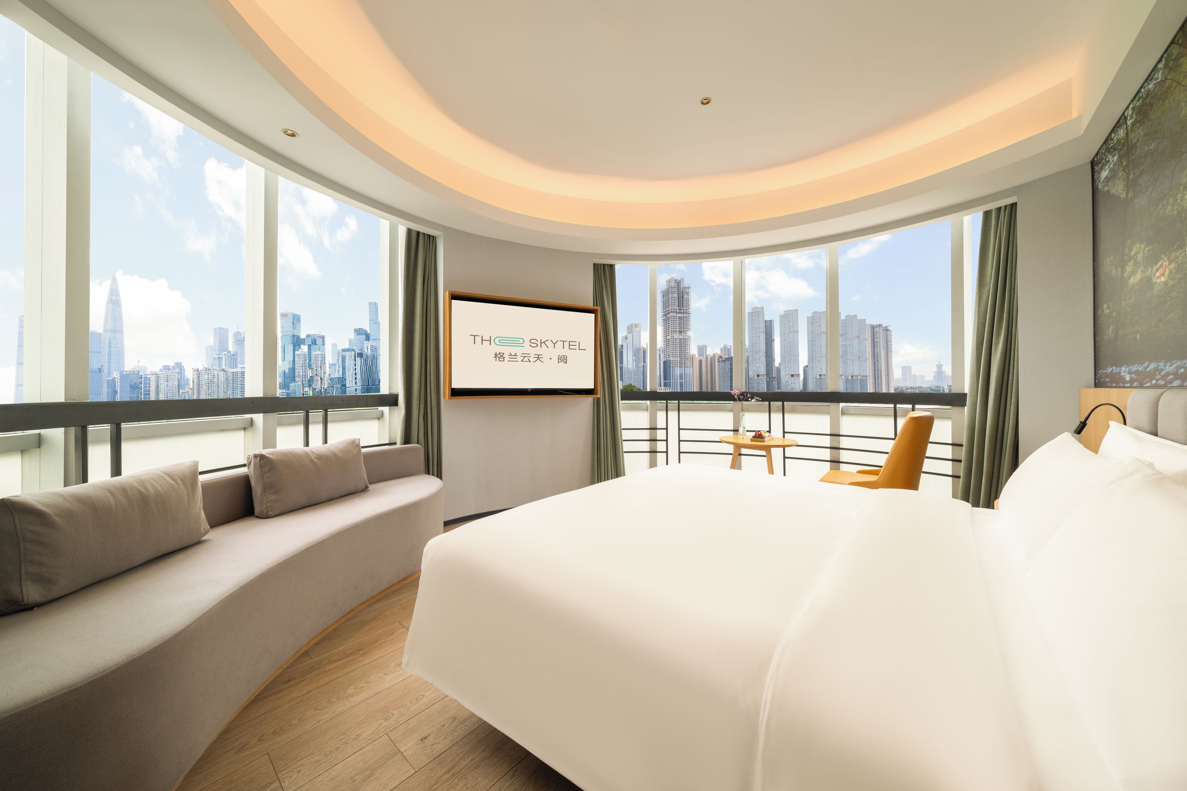 A modern hotel room with a large bed, a seating area, and a city view.