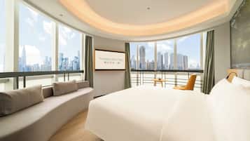 Una habitación de hotel moderna con una cama grande, una zona de estar y vistas a la ciudad.
