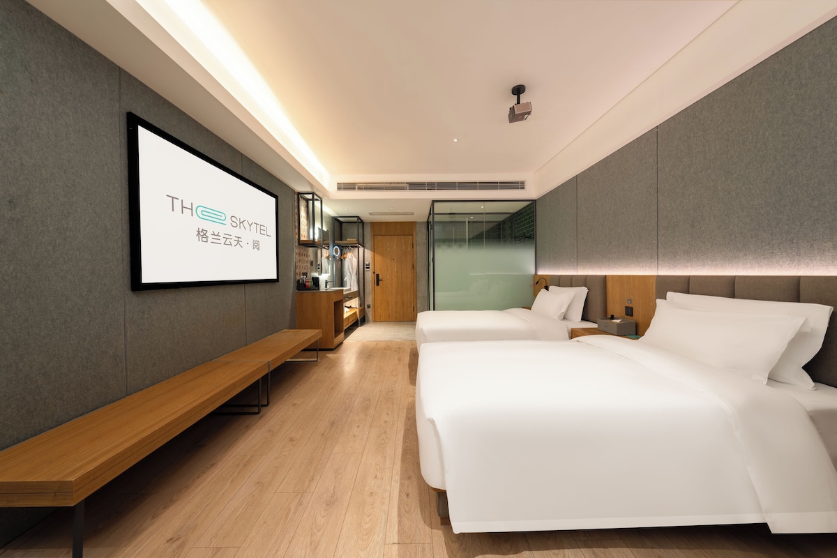 A hotel room with two beds, a bench, a TV screen, and a mirror.