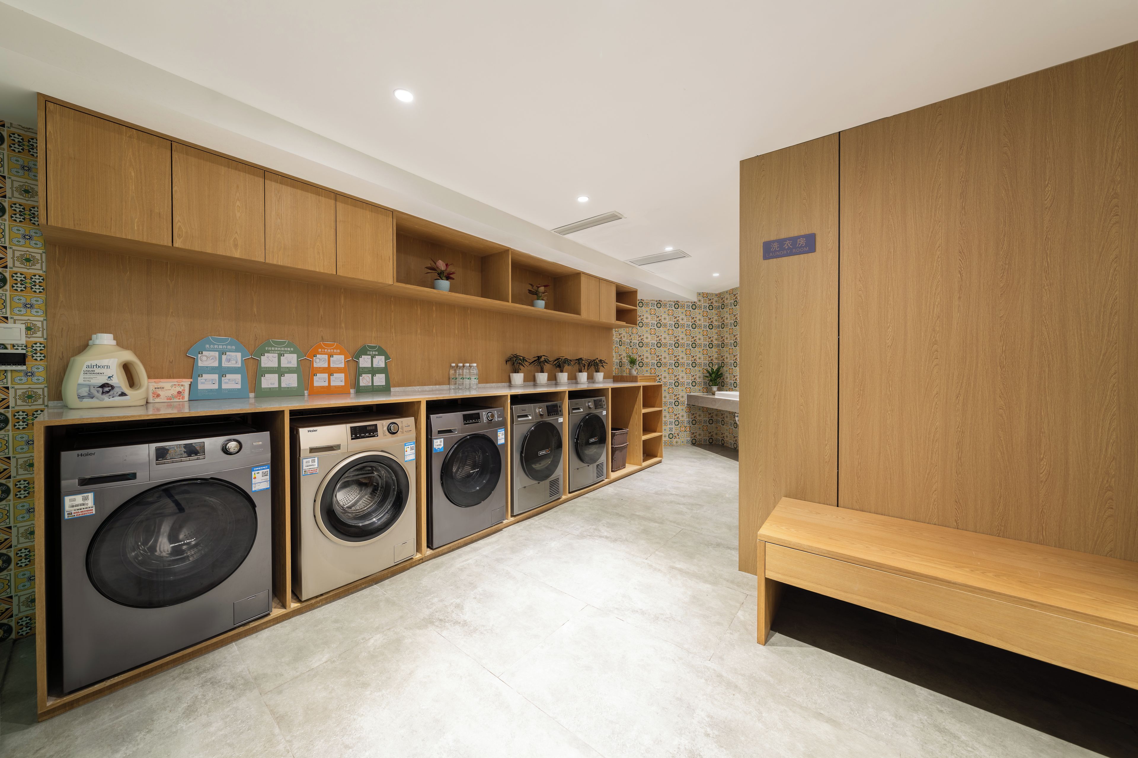 A laundry room with multiple washing machines, wooden shelving, and a bench.