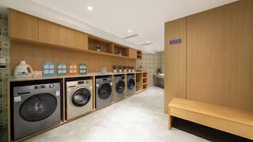 A laundry room with multiple washing machines, wooden shelving, and a bench.