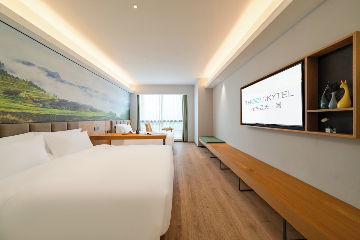 A hotel room with a large bed, a desk, a television, and a mural on the wall.