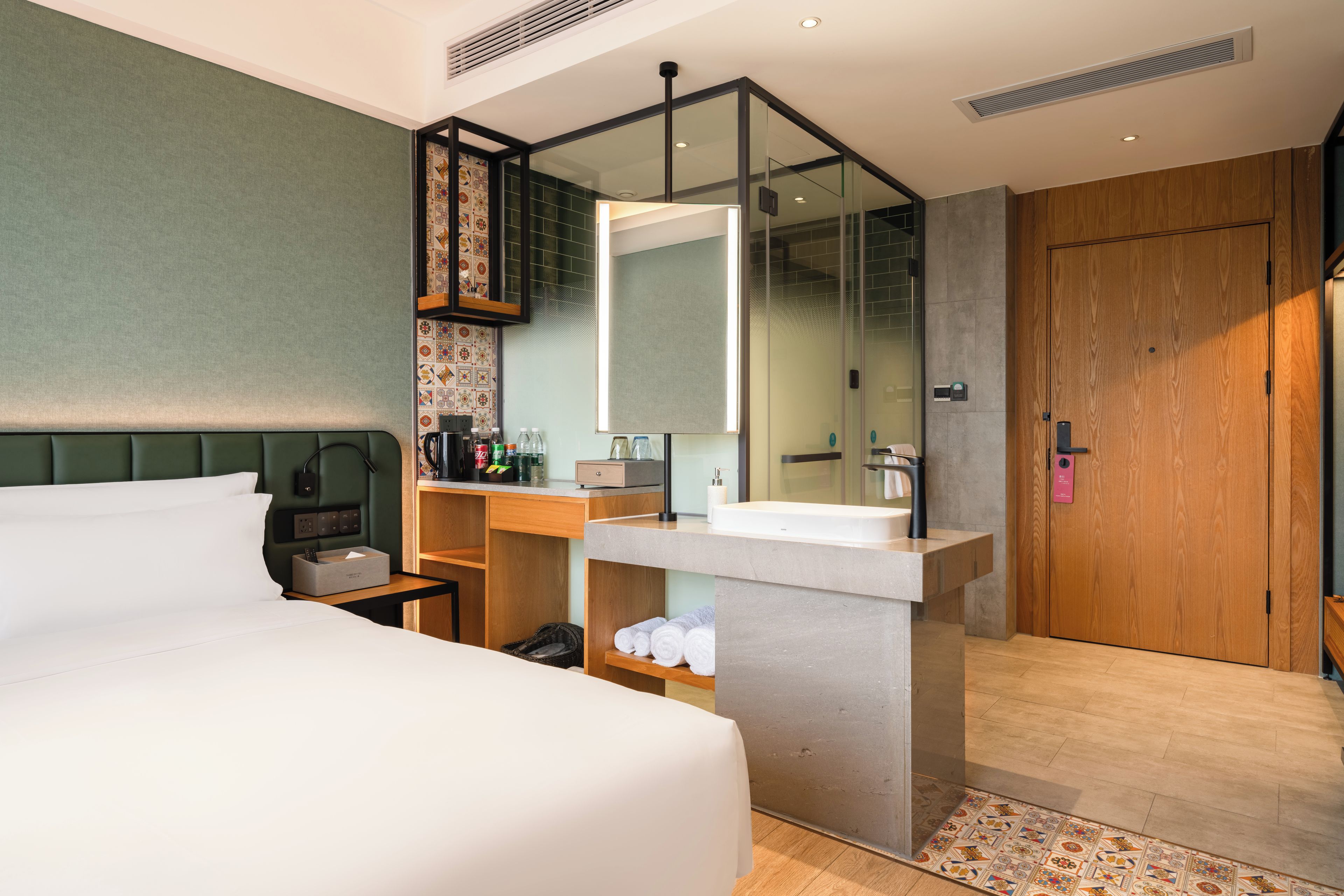 A modern hotel room with a large bed, a bathroom with a glass shower enclosure, and a wooden wardrobe.