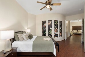 Une chambre à coucher avec un lit, des lampes de chevet, un ventilateur de plafond et une vue sur une pièce adjacente.