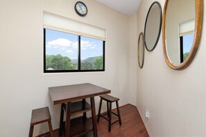 A room with a wooden table and two stools, a window with a view of trees and hills, and two wall-mounted mirrors. - Les Clés ~ Sedona (Sedona)