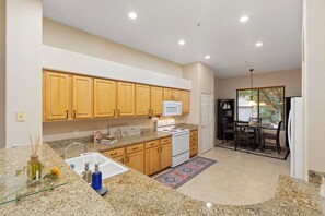 A modern kitchen with granite countertops, wooden cabinets, a white stove, and a dining area with a table and chairs. - Les Clés ~ Sedona (Sedona)