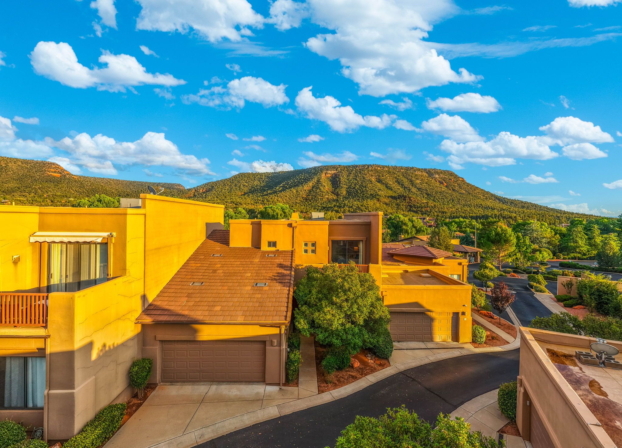 Un barrio residencial con casas amarillas, cielo despejado y un paisaje montañoso al fondo.