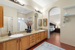 Une salle de bain moderne avec un meuble-lavabo à deux vasques, des armoires en bois, un grand miroir et un espace douche.