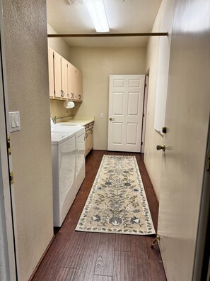 A narrow hallway with a wooden floor, a white door, and a kitchen area with cabinets and a countertop. - Les Clés ~ Sedona (Sedona)