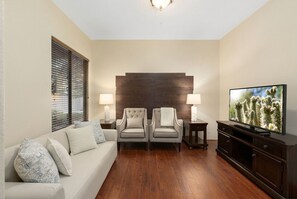 Een woonkamer met een bank, twee fauteuils, een televisie en een wandlamp.