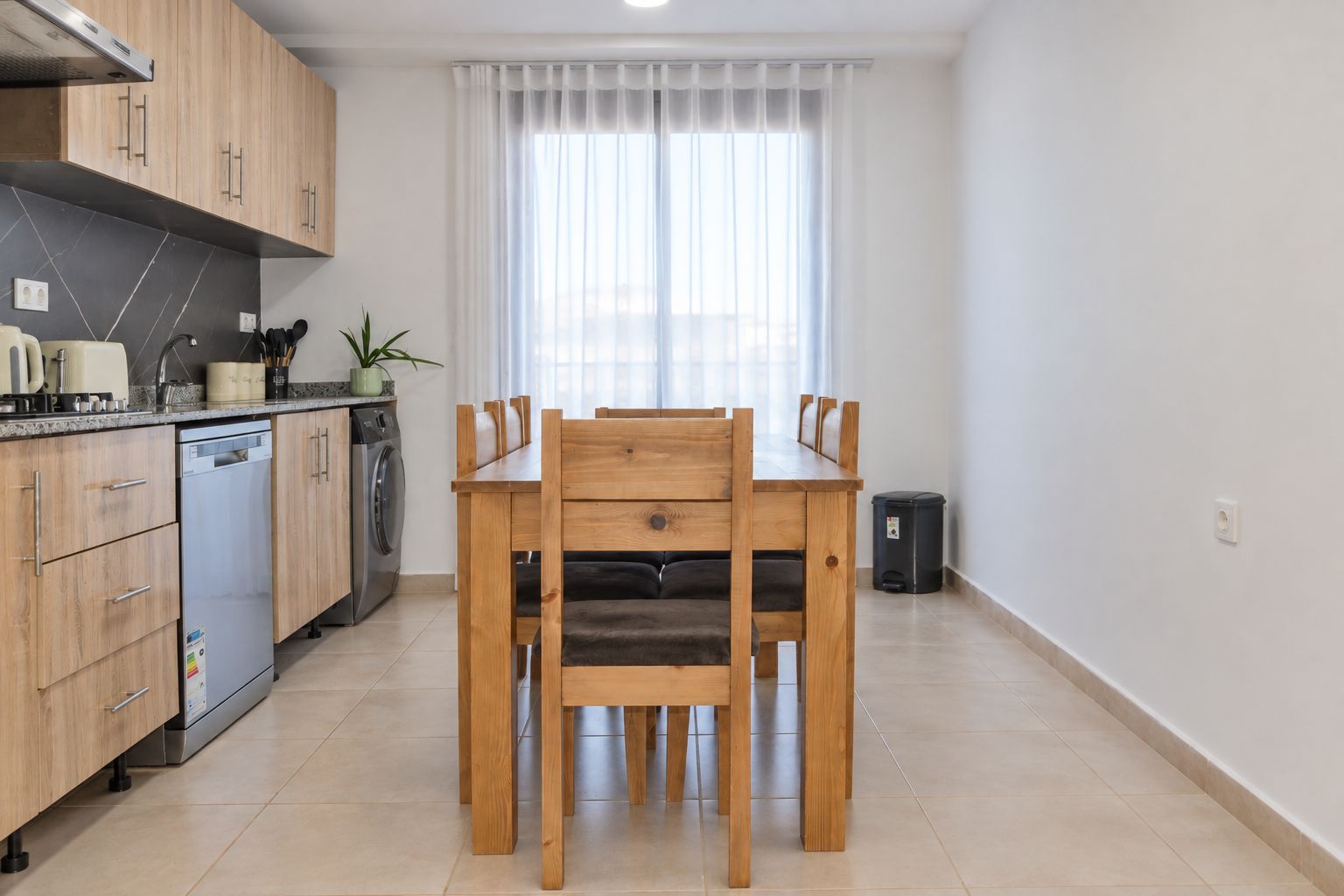 A modern kitchen with wooden cabinets, a built-in dishwasher, and a dining table with chairs.