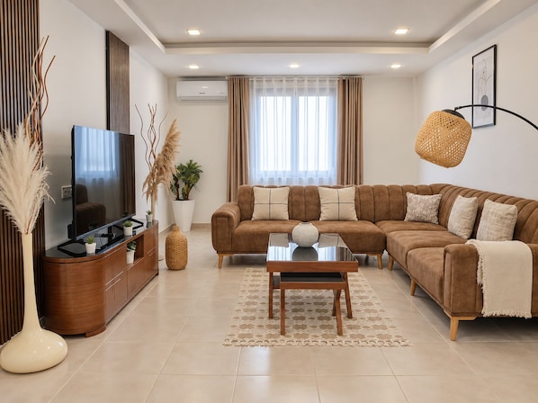 A modern living room with a sectional sofa, a flat-screen TV, a wooden cabinet, and a decorative vase.