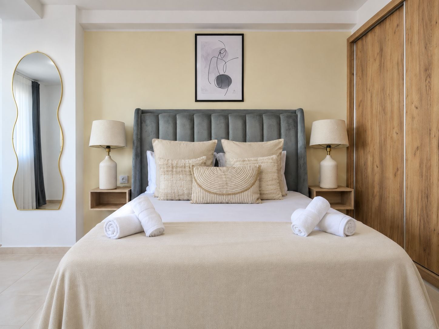 Una habitación de hotel con una cama grande, dos lámparas de noche, un espejo, una obra de arte enmarcada y un armario.