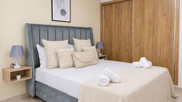 A bedroom with a bed, pillows, a bedside table with a lamp, a wooden wardrobe, and a framed picture on the wall.