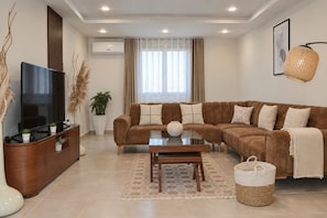 A modern living room with a sectional sofa, a flat-screen TV, a coffee table, and a decorative plant.