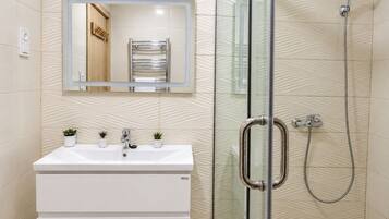 A modern bathroom with a glass shower enclosure, a white sink with two plants, and a mirror above the sink.
