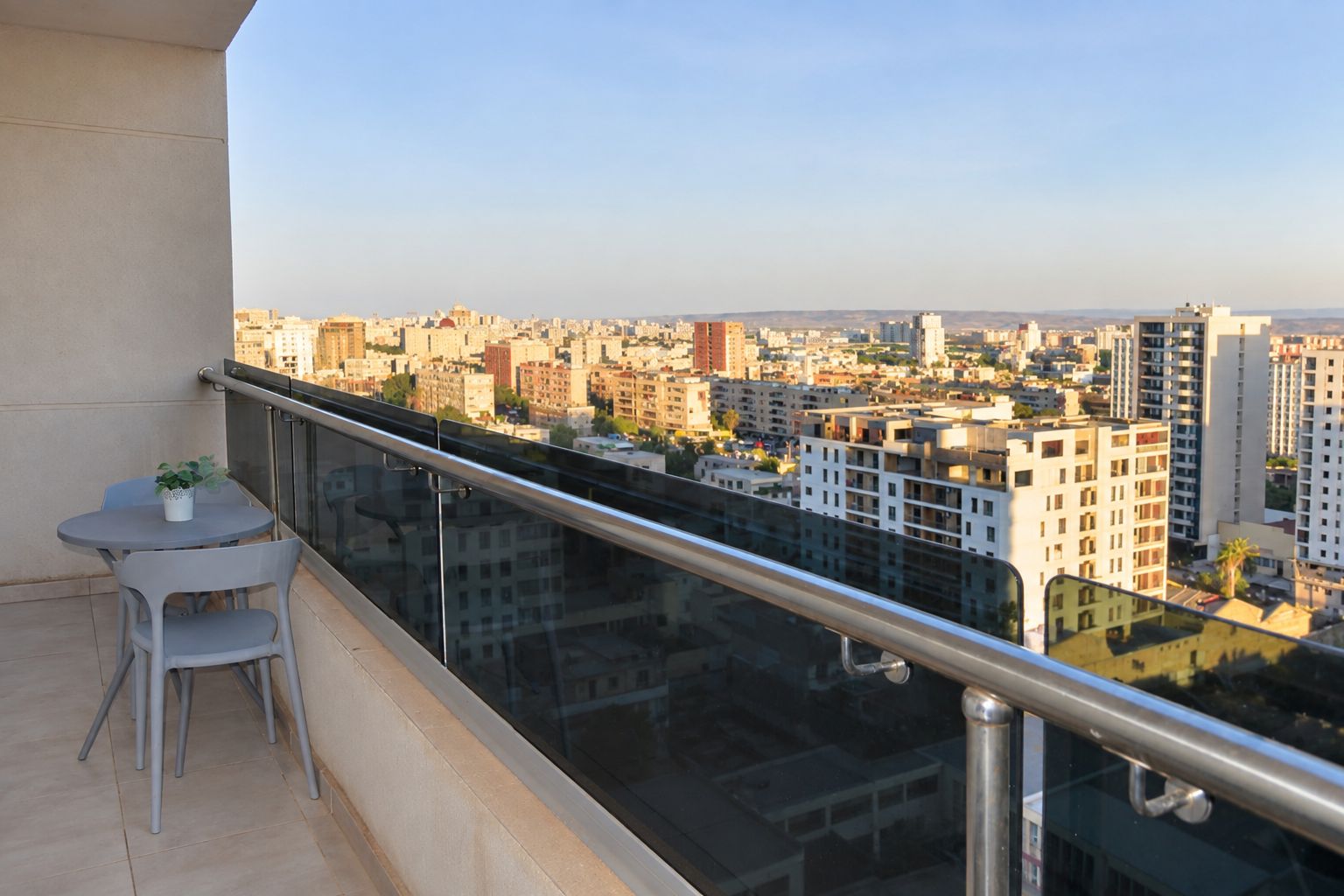 Un balcón con barandilla de vidrio con vistas a un paisaje urbano con diversos edificios.