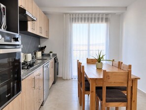 A modern kitchen with a built-in oven, microwave, and gas stove. There is a dining table with chairs and a potted plant on the table.