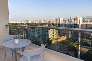 A balcony with a table and chairs, overlooking a cityscape with various buildings.