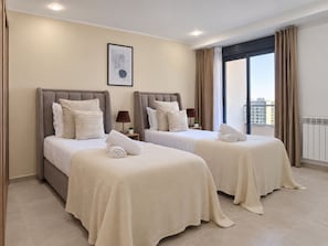 A hotel room with two beds, a window with curtains, a framed picture on the wall, and a radiator.