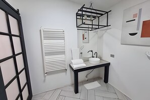 Casa de banho moderna com lavatório branco, bancada preta e um porta-toalhas.