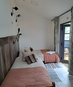 Quarto com duas camas, cabeceira de madeira e vista através de uma porta aberta.