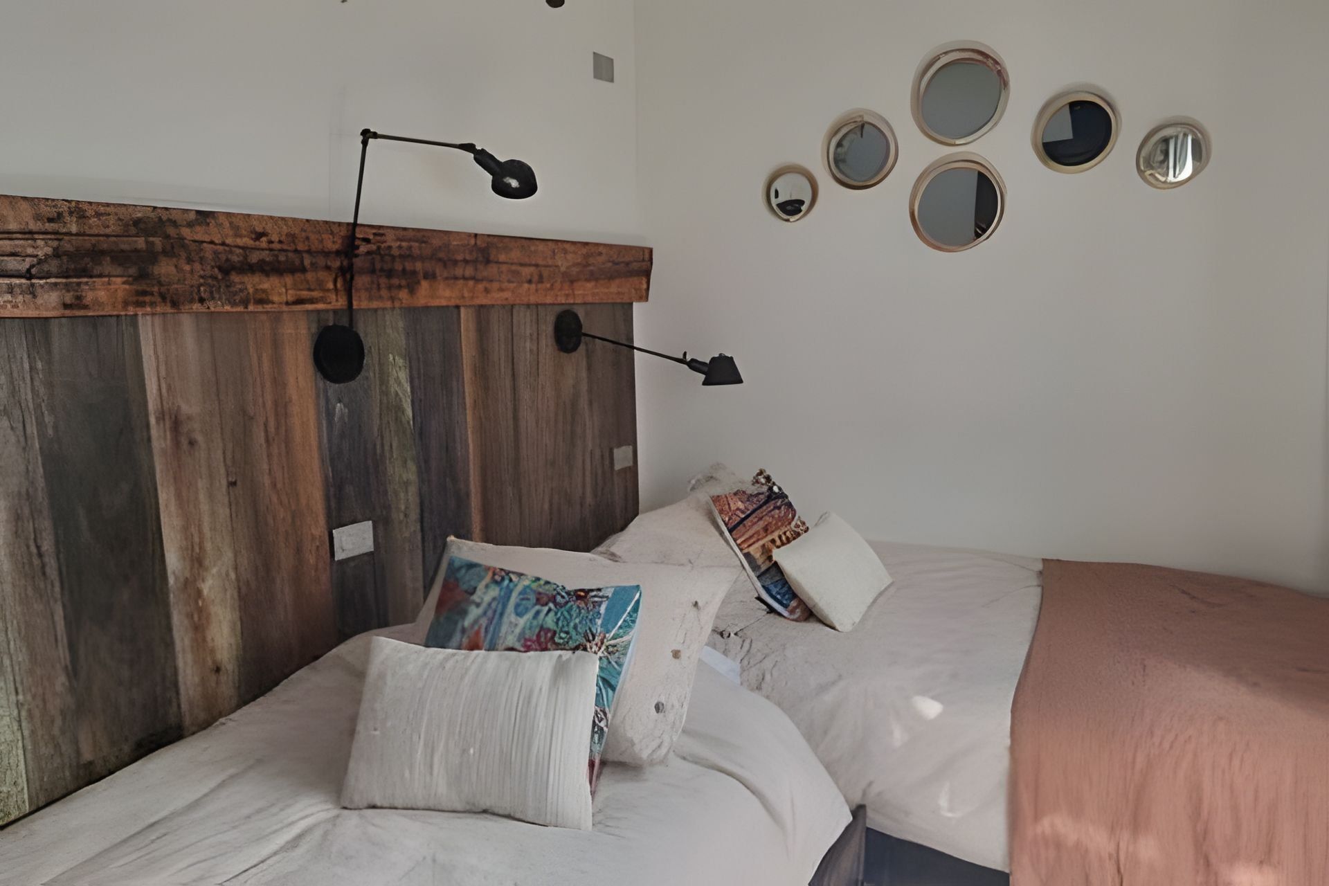 Un dormitorio con cabecera de madera, varios almohadones, lámpara de noche y espejos en la pared.