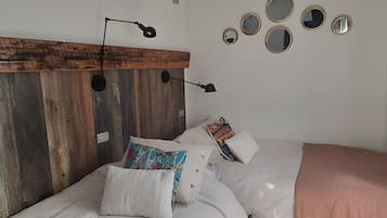 Un dormitorio con cabecera de madera, varios almohadones, lámpara de noche y espejos en la pared.