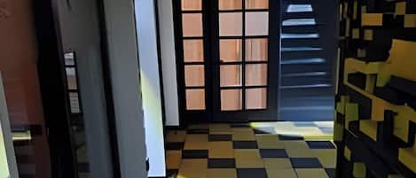Un pasillo con piso a cuadros, una puerta con ventanal y una pared con diseño geométrico.