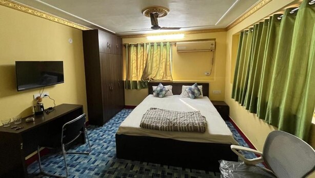 A hotel room with a bed, a desk, a television, and a ceiling fan. - PLATINUM IN GUEST HOUSE (Barasat)