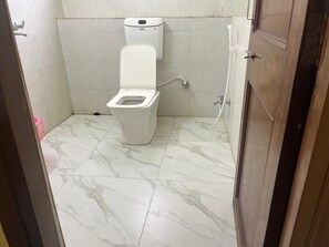 A bathroom with a toilet, a wall-mounted bidet, and a marble floor.