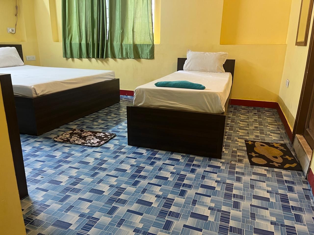 A room with two beds, a patterned floor, and a green curtain.