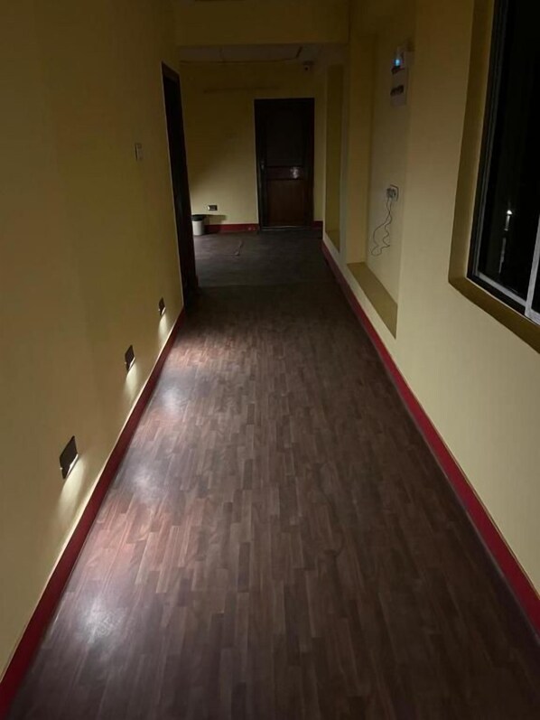 A corridor with a wooden floor and a red trim, leading to a door at the end.