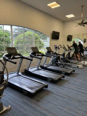 A gym with multiple treadmills, a ceiling fan, and large windows with a view of greenery. - Seasonal Rental in Cape Coral, FL (Cape Coral)