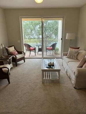 A living room with a sofa, armchairs, a coffee table, and a balcony with chairs and a table. - Seasonal Rental in Cape Coral, FL (Cape Coral)