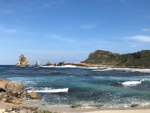 Eine Küstenlandschaft mit blauem Himmel, Felsenformationen und einem Leuchtturm auf einem Hügel.