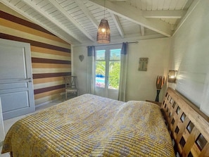 Ein Schlafzimmer mit einem Bett, einem Fenster mit Vorhängen, einem hölzernen Kopfteil und einer Decke mit sichtbaren Balken.