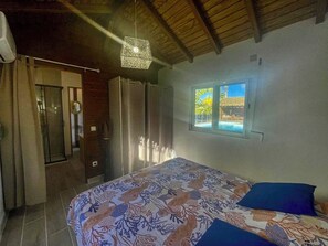 A bedroom with a bed, a window with a view, and a ceiling light fixture. - Just 650 meters from the ocean! 4-bedroom villa with a large pool and bar area (Saint-François)