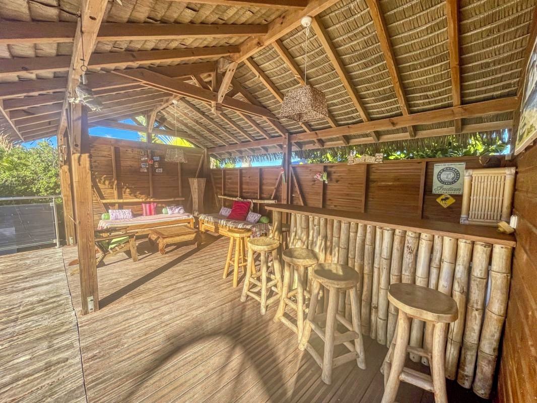 Eine Holzterrasse mit Barbereich, Hockern und einem Tisch mit Kissen.
