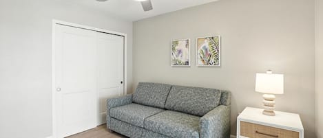 A room with a grey sofa, a white bedside table with a lamp, and two abstract paintings on the wall.