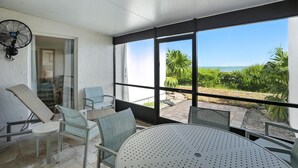 Ein sonniger Balkon mit Tisch und Stühlen, einem Ventilator und Blick auf Grünflächen und Wasser.