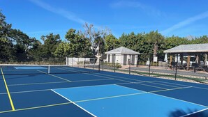 Ein Tennisplatz mit mehreren Spielfeldern, umgeben von Bäumen und schattigen Bereichen.