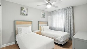 Ein Hotelzimmer mit zwei Einzelbetten, einem Deckenventilator und einem fensterbelaubten Fenster.