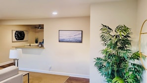 A room with a white sofa, a lamp, a clock, a framed picture, and a large plant.